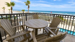 A balcony with a table and chairs, overlooking a beach with palm trees and a flag.