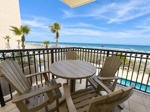 Un balcon avec une table et des chaises, donnant sur une plage bordée de palmiers et sur laquelle flotte un drapeau.