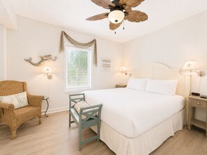 A bedroom with a bed, a chair, a nightstand, a wall-mounted lamp, a ceiling fan, and a window with blinds.