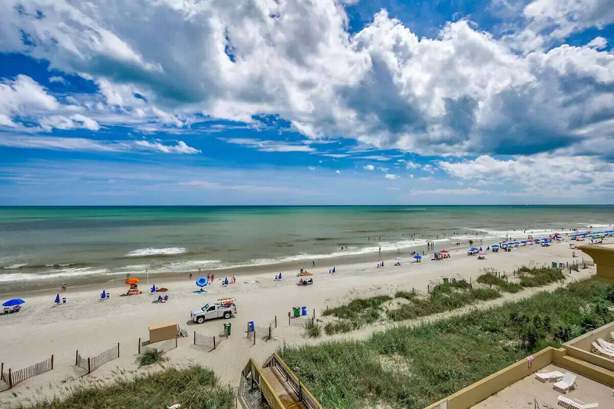 A beach with umbrellas, lounge chairs, and a boardwalk.