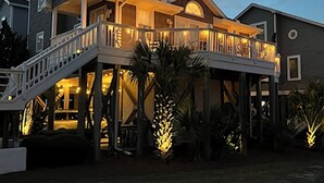 Una casa a due piani con un balcone, un patio in legno e illuminazione esterna.