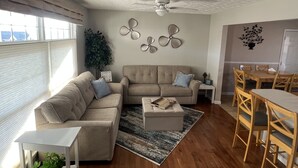 A living room with a sofa, ottoman, and coffee table, a dining area with a table and chairs, a ceiling fan, and wall decor. - Porch sunset on the lake, 1/2 mile from Beaver Creek Marina! (Monticello)