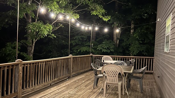 A wooden deck with string lights, a table, and chairs. - Porch sunset on the lake, 1/2 mile from Beaver Creek Marina! (Monticello)