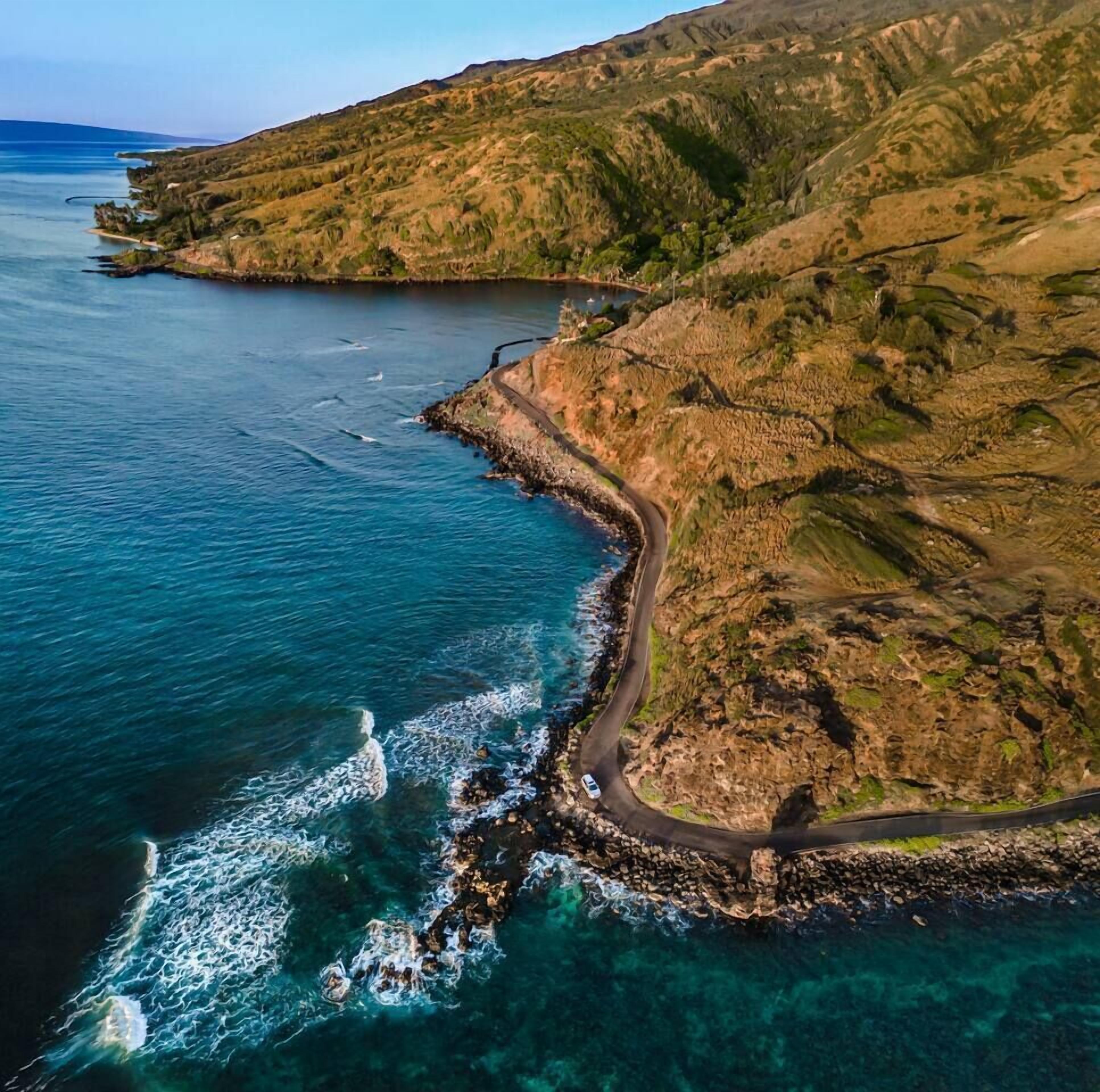 Una carretera costera serpentea a lo largo de una costa rocosa con aguas azules cristalinas y un paisaje montañoso.