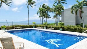 A swimming pool with a dolphin logo, surrounded by palm trees and a view of the ocean. - September Sale! Molokai Island Retreat (Kaunakakai)