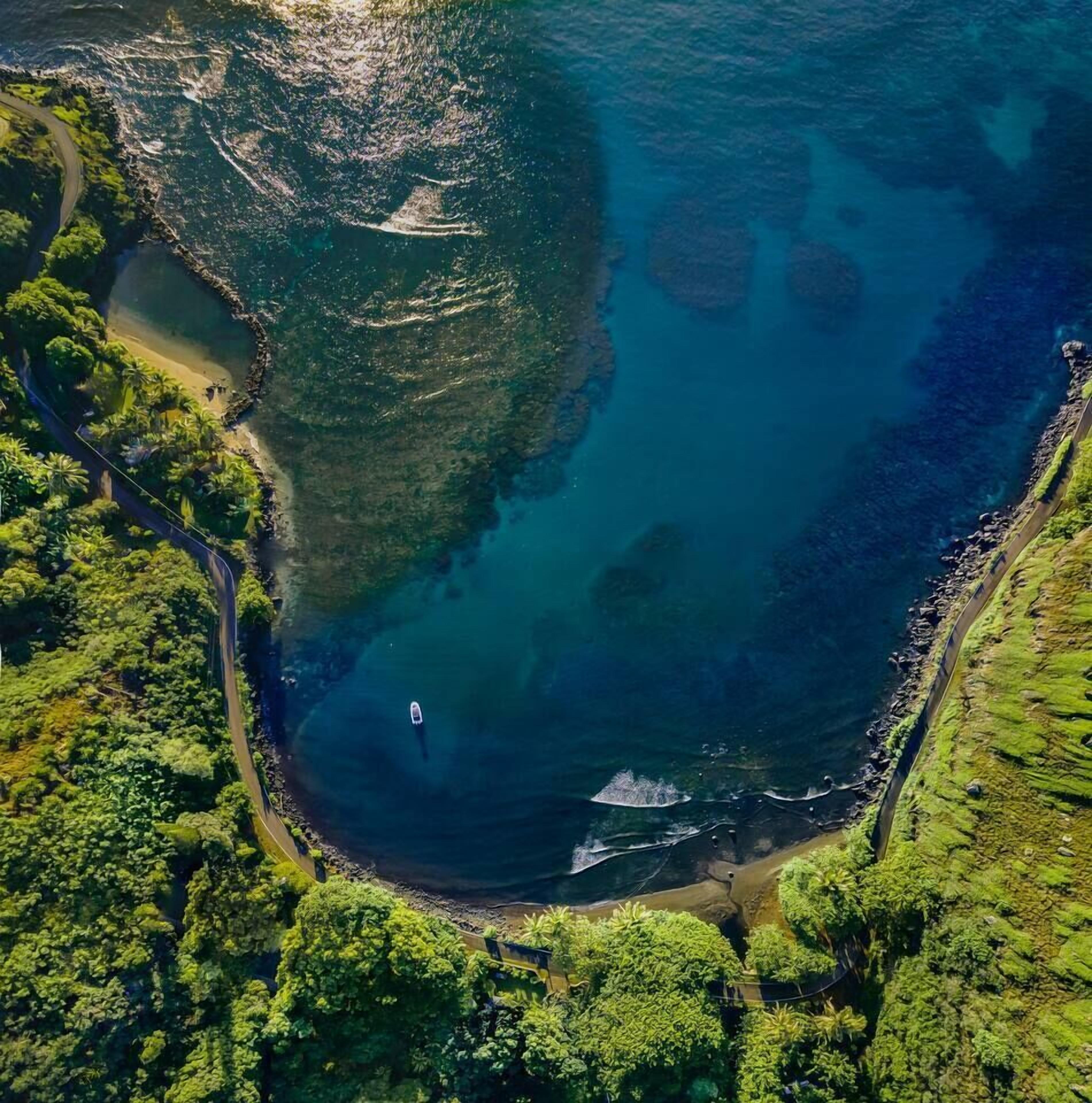 Vista aérea de una zona costera con una carretera serpenteando a lo largo de la costa, un barco en el agua y vegetación densa alrededor.