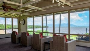 A room with wicker furniture and large windows overlooking a body of water. - September Sale! Molokai Island Retreat (Kaunakakai)