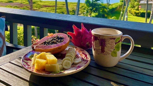 A tropical view with a table set with a fruit plate, a dragon fruit, and a mug. - September Sale! Molokai Island Retreat (Kaunakakai)