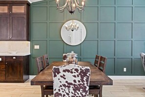 Un comedor con una mesa de madera, sillas, una araña, un espejo y una pared revestida de paneles verdes.