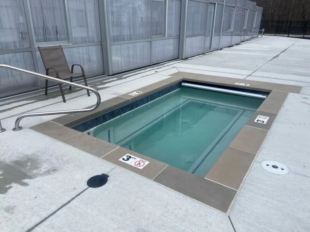 A small indoor pool with a metal ladder and a chair, surrounded by a tiled deck.
