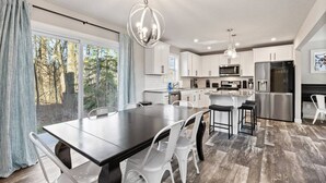 Een moderne keuken met witte kasten, roestvrijstalen apparatuur, en een eethoek met een donkere tafel en witte stoelen.