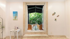 A room with a large window, a white table with decorative items, and a painting on the wall.