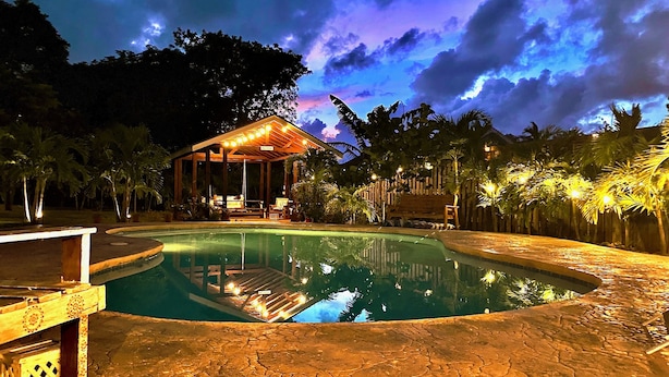 A nighttime pool area with a covered seating area and a wooden deck surrounding the pool.