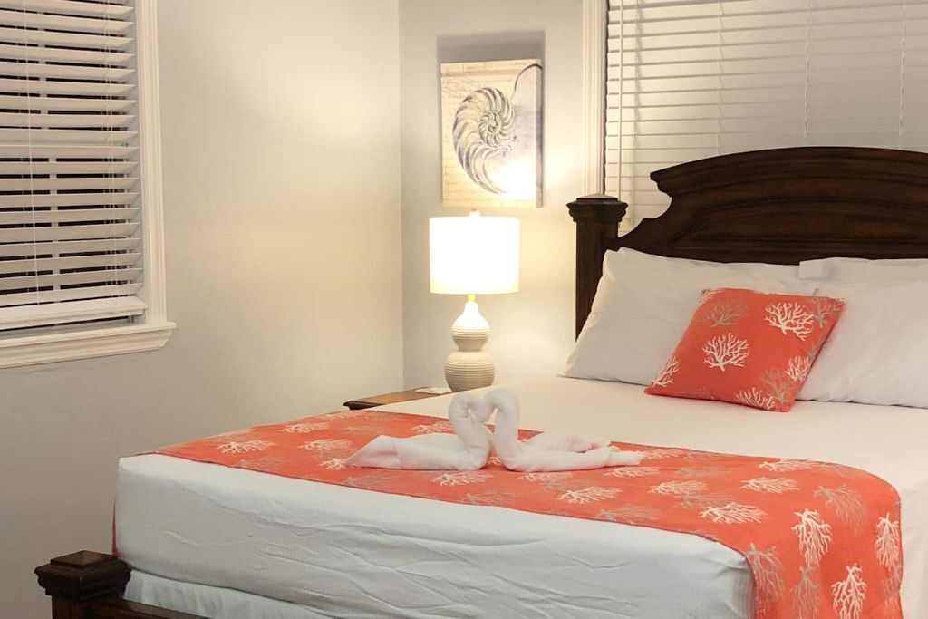 A neatly made bed with a red and white patterned bedspread, a wooden headboard, and a single white pillow.