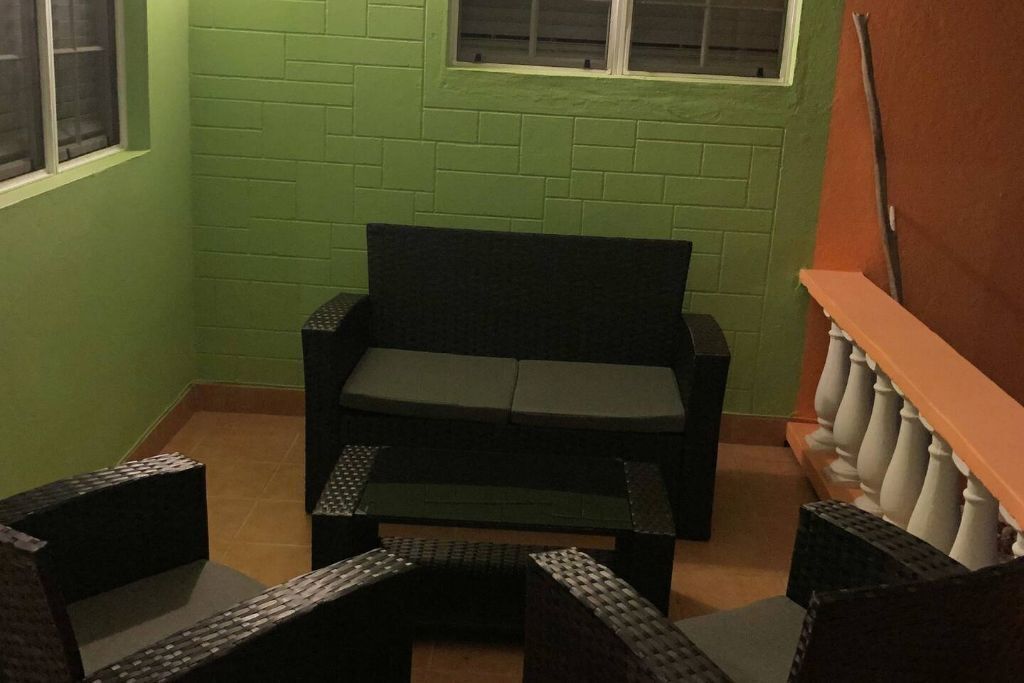 Un petit balcon fermé, avec un mur en briques vertes, une chaise noire et un banc en bois.