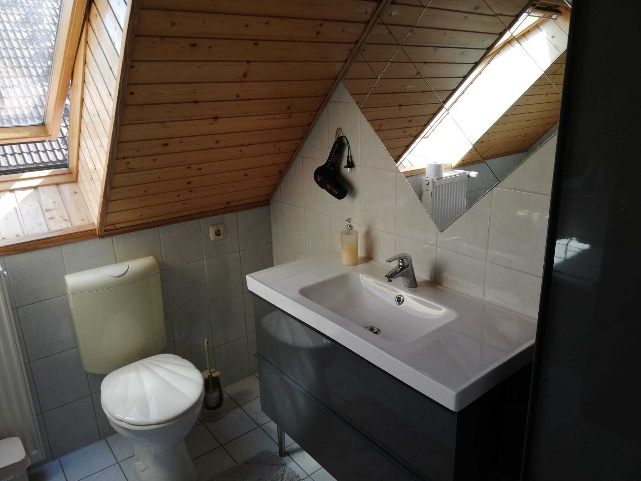 Une salle de bain moderne avec des toilettes blanches, un lavabo avec un miroir et une fenêtre au-dessus du lavabo.