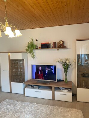 Una sala de estar moderna con un televisor de pantalla plana, estantes de madera, un aparador de vidrio y un sofá blanco.