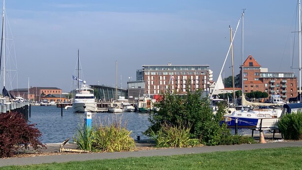 A marina with boats docked, a building with a red roof, and a modern structure with large windows.