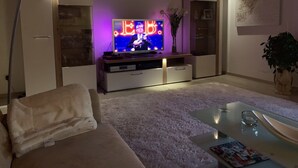 A living room with a flat-screen TV, a sofa, a coffee table, and a bookshelf.
