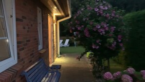 A brick building with a bench and a pathway leading to a garden with pink flowers.