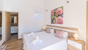 A hotel room with two beds, a wooden headboard, a nightstand with a lamp, and a painting of flowers on the wall.