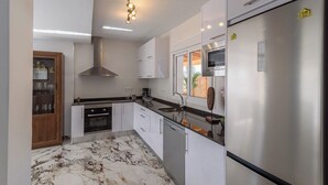 Een moderne keuken met witte kasten, een roestvrijstalen koelkast, een inbouwoven en een marmeren vloer.