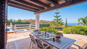 Zona pranzo all'aperto con piscina, pergola in legno e vista sull'oceano.