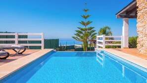 Una piscina cristallina con un bordo bianco, un muro in pietra e vista sul mare.