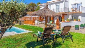 A poolside area with lounge chairs, a thatched umbrella, and a building with balconies. - Villa Matella Vélez-Málaga by Ruralidays (Málaga)