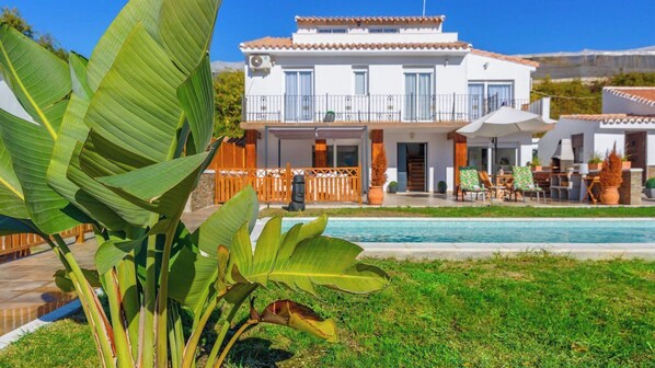Une maison à deux étages avec une piscine, entourée de verdure et d’une clôture en bois.