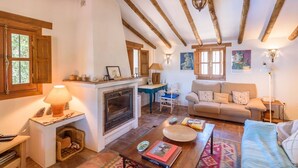 A cozy living room with a fireplace, wooden beams, a sofa, and a coffee table. - Casa Angelica Cómpeta by Ruralidays (Málaga)