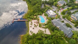 An aerial view of a resort with a swimming pool, a dock, and surrounding greenery.