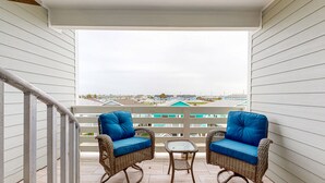 A balcony with wicker chairs and a small table, overlooking a residential area. - Shared Heated Pool, Observation Deck, Golf Cart Included, Pet Friendly (Port Aransas)