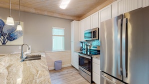 A modern kitchen with a marble countertop, stainless steel appliances, and wooden flooring. - Shared Heated Pool, Observation Deck, Golf Cart Included, Pet Friendly (Port Aransas)
