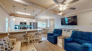 A spacious living area with a large blue sofa, a wooden dining table, and a kitchen with modern appliances. - Shared Heated Pool, Observation Deck, Golf Cart Included, Pet Friendly (Port Aransas)