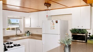A compact kitchen with white cabinets, a stainless steel refrigerator, a gas stove, a sink, and a microwave.