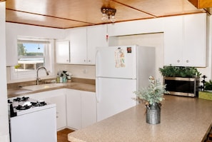 A compact kitchen with white cabinets, a stainless steel refrigerator, a gas stove, a sink, and a microwave. - Quiet Lakefront Cabin · Private Dock and Firepit (Bath)