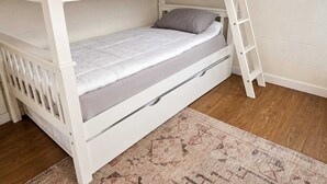 A bunk bed with a ladder, a single bed below, and a patterned rug on the floor.
