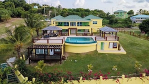 Une grande maison à deux étages dotée d’une piscine, de plusieurs terrasses et d’un jardin bien entretenu.