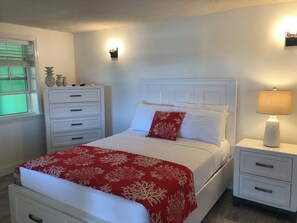Ein ordentlich eingerichtetes Schlafzimmer mit Bett, Nachttisch, Kommode und einem Fenster mit Rollläden.