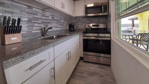 Eine kleine Küche mit weißen Schränken, einer Arbeitsplatte aus Granit, einer Edelstahl-Spüle, einer Mikrowelle und einem Backofen.