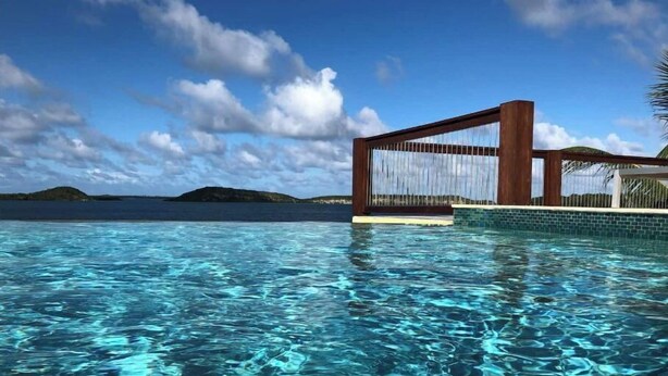 Een helder zwembad met een houten terras en uitzicht op de oceaan.