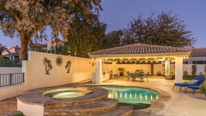 Un patio trasero con piscina, jacuzzis, un porche cubierto y mobiliario de exterior.
