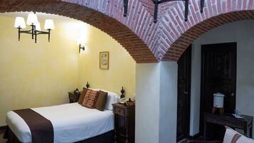 Quarto de hotel com cama, mesa de cabeceira, luminária, quadro na parede e uma porta.