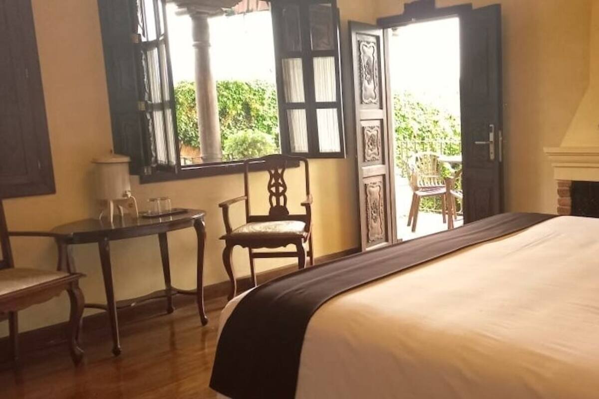 Ein Schlafzimmer mit einem großen Bett, einem kleinen Tisch, einem Sessel und einem Kamin.