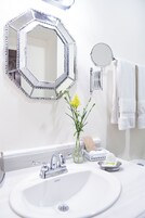 A bathroom with a white sink, a hexagonal mirror, a round mirror, and a vase with yellow flowers.