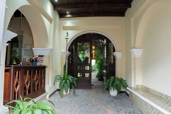 A hallway with a wooden reception desk, potted plants, and a tiled floor.