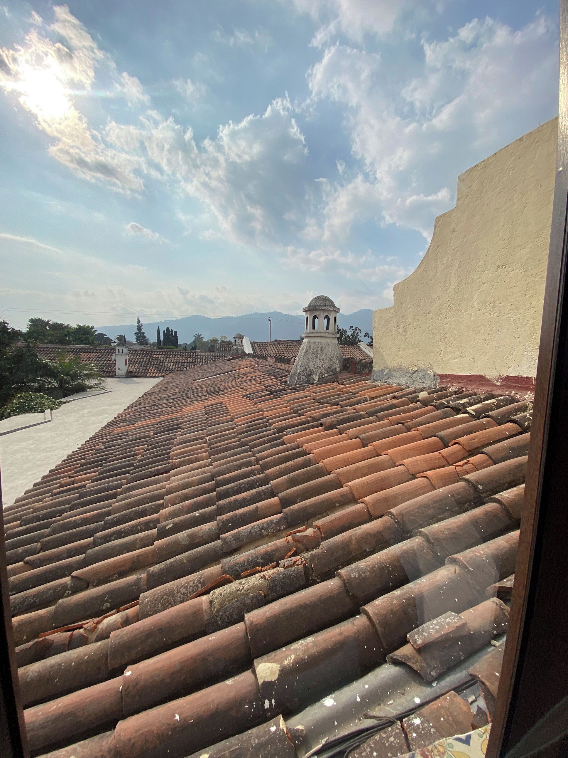 A rooftop with terracotta tiles, a small tower-like structure, and a clear sky with clouds.