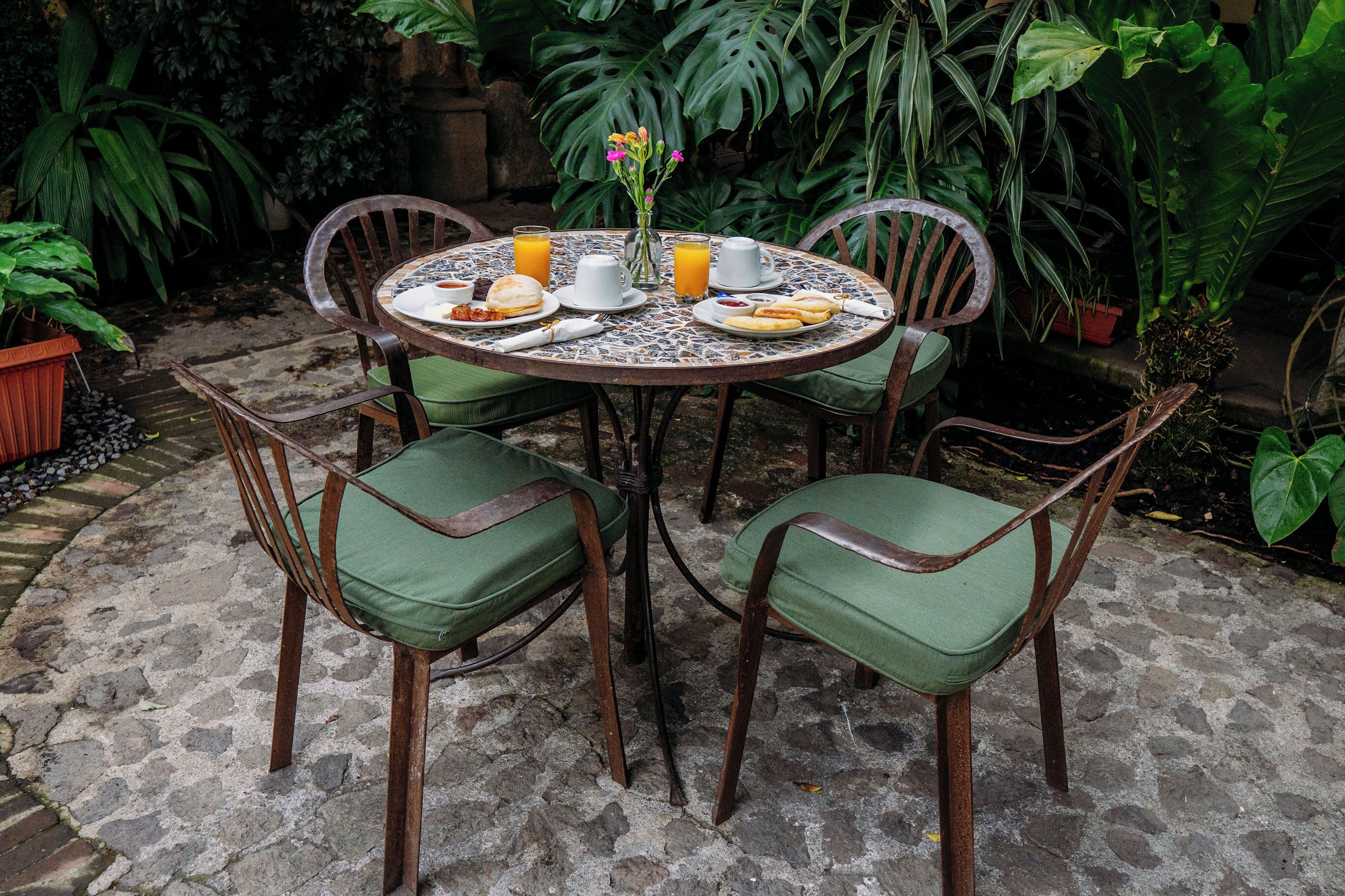 Een ronde tafel met stoelen, een vaas met bloemen en een ontbijtje.