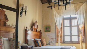 Une chambre avec deux lits, des têtes de lit en bois, un lustre, une fenêtre avec des rideaux et un miroir.